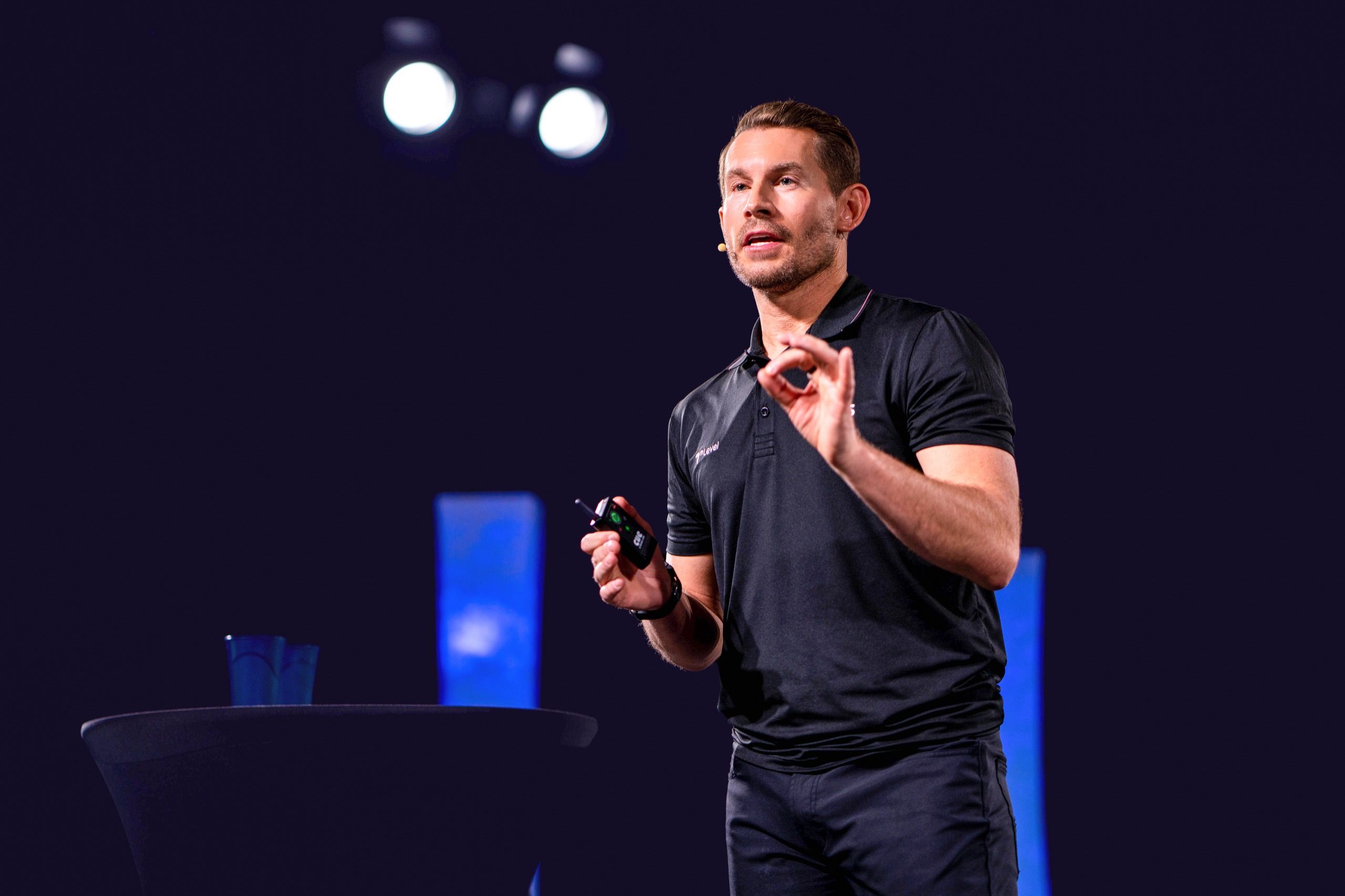 Jeremy Miner on stage in a black polo, mid-explanation, holding a slide clicker