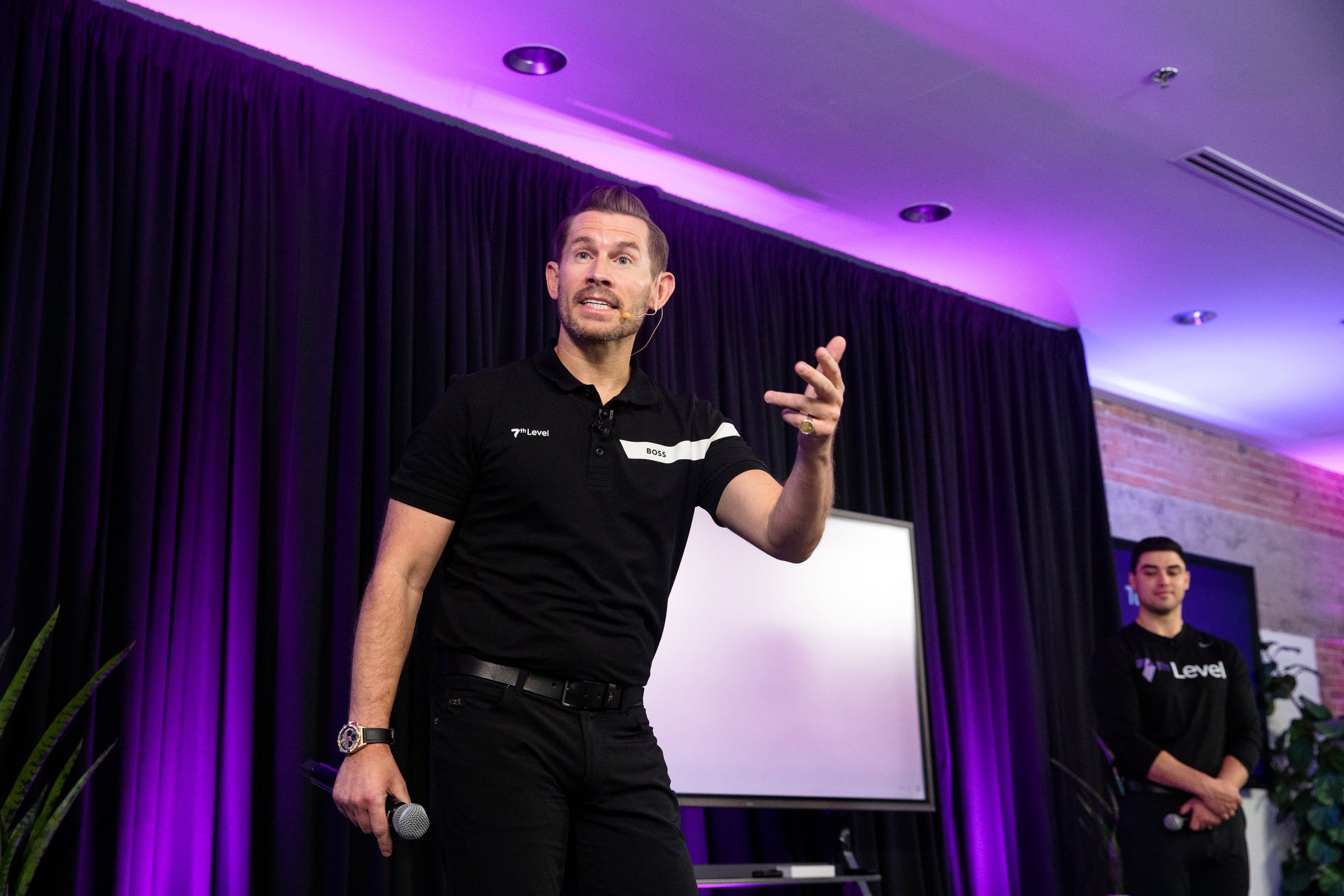 Jeremy Miner on stage under purple lighting, gesturing to the room as he speaks