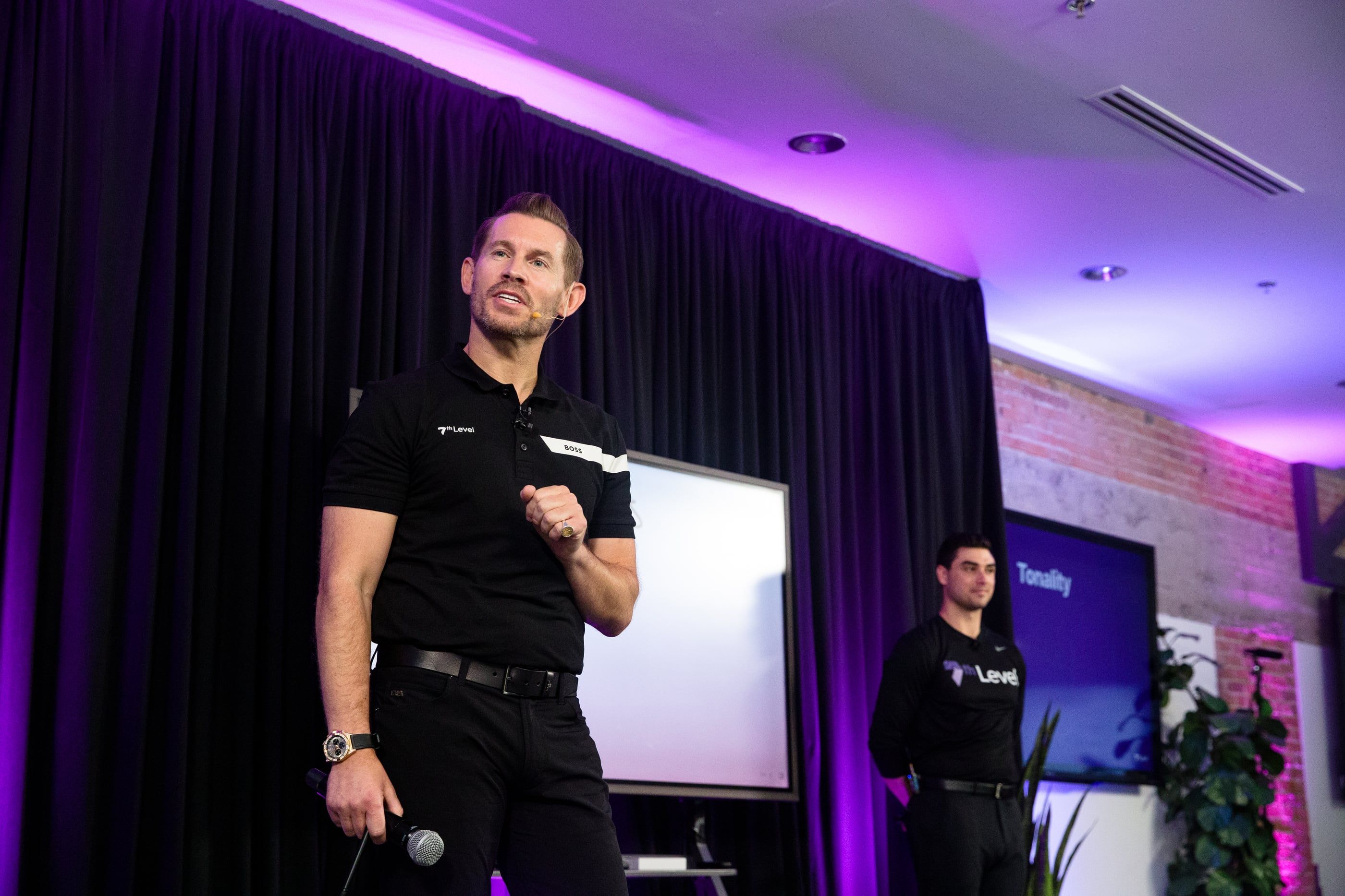 Jeremy Miner speaking on stage under purple lighting, a team member standing behind him