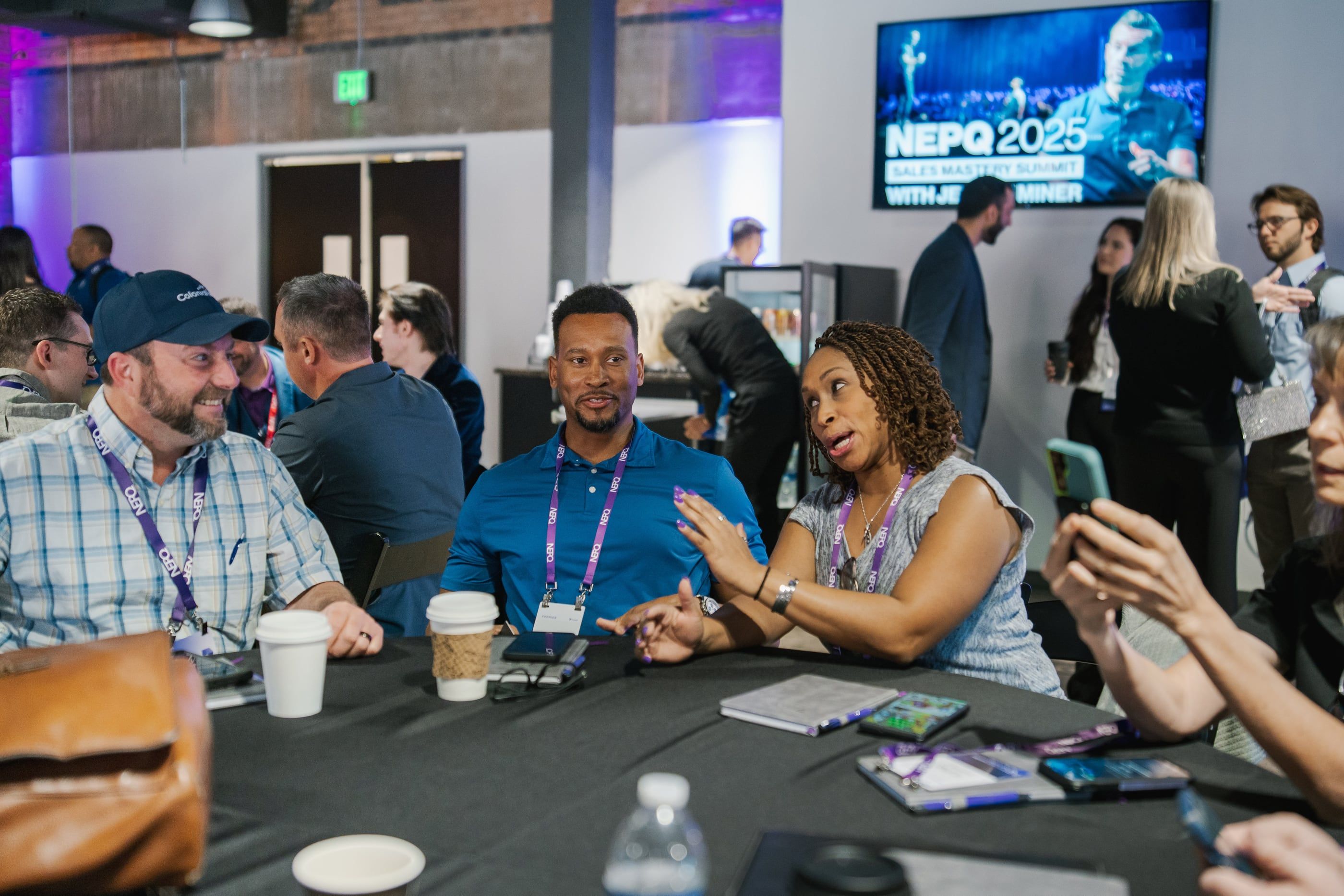 Three attendees in conversation across a table between sessions